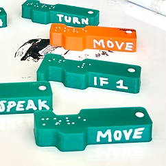 cost.webp Completed 3D printed code blocks with Braille and English labels in green and orange